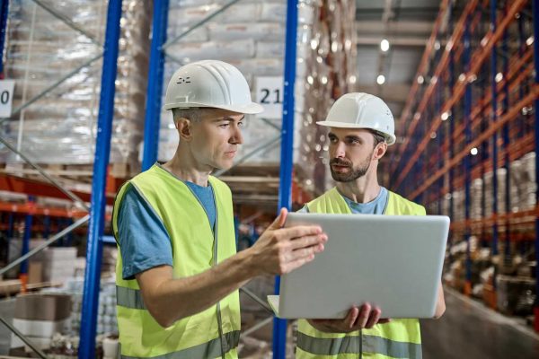 two-men-overalls-with-laptop-talking-warehouse